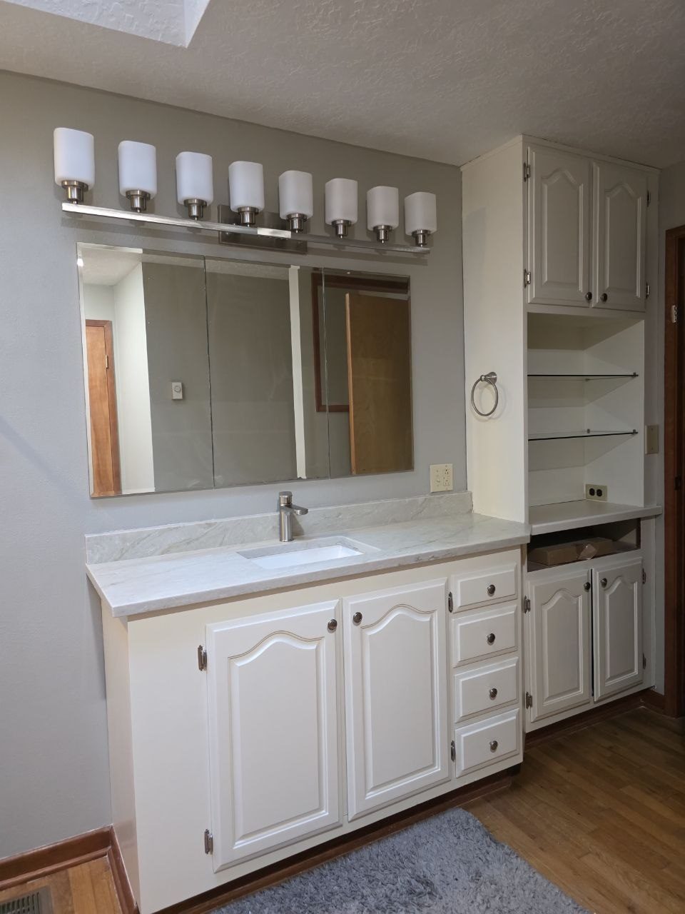 Primary bathroom vanity after remodel — new white cabinetry, quartz counter, and updated lighting